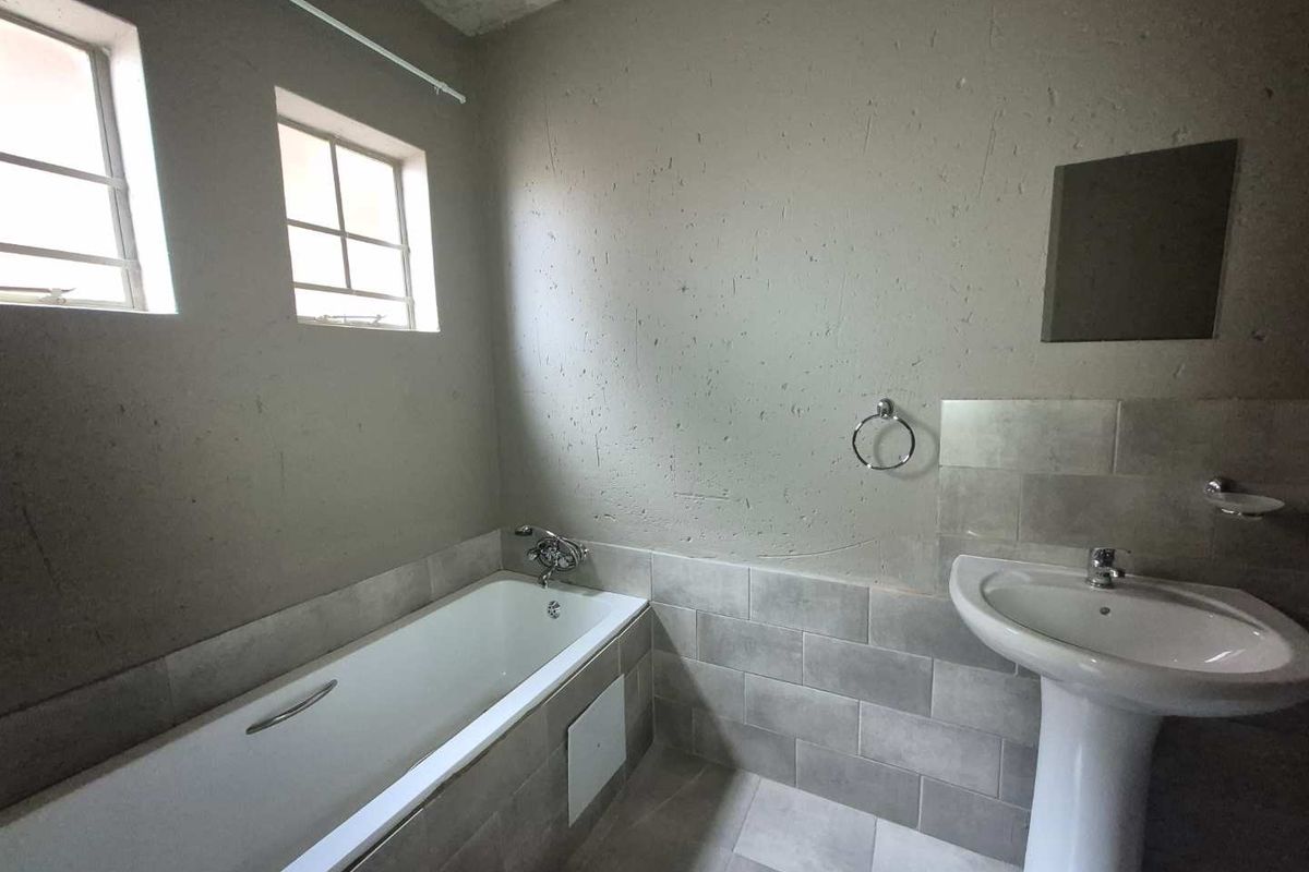 A basic bathroom featuring a bathtub, pedestal basin, and tiled finishes, currently requiring cosmetic updates to the wall surfaces and ceiling.