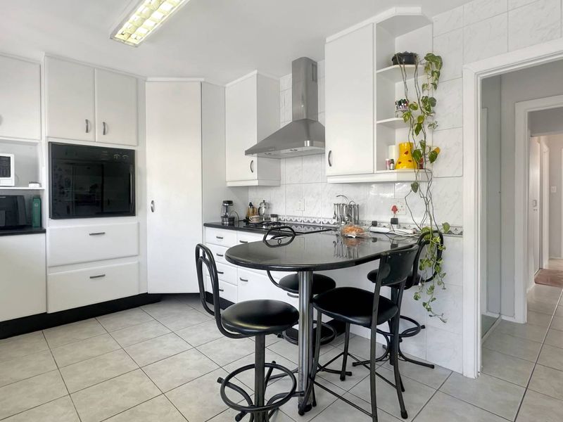 A functional kitchen featuring white built-in cabinetry, a stainless steel extractor fan, built-in oven, tiled backsplash, and tiled flooring.
