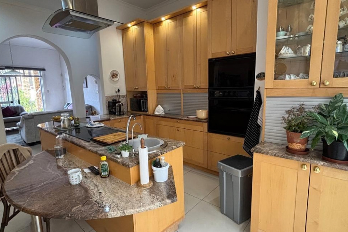Spacious kitchen featuring light wood cabinetry, granite countertops, built-in oven, and a central island with integrated hob and breakfast bar.