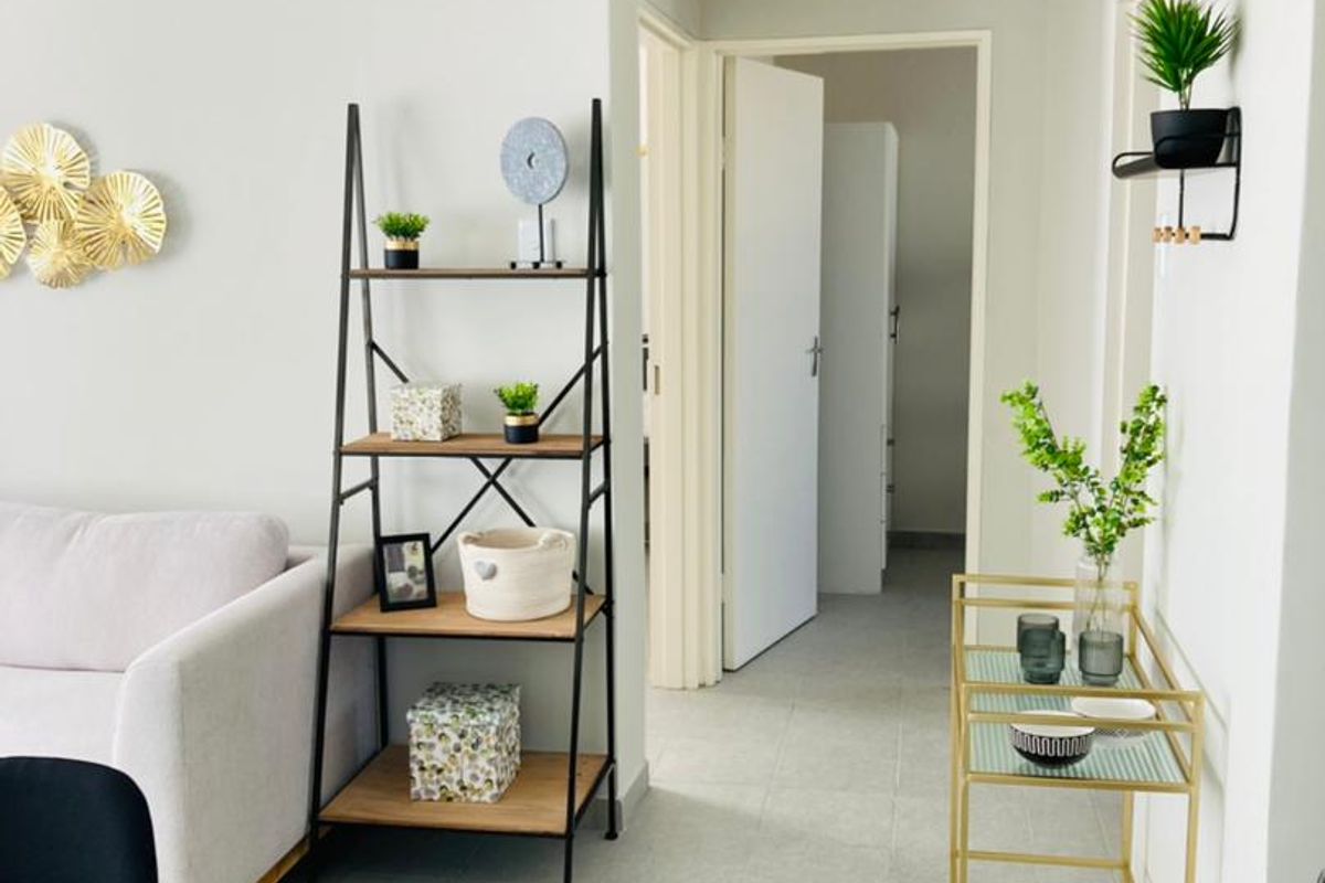 A bright and well-maintained living area featuring neutral tiled flooring and clean wall finishes, leading into a hallway with access to adjacent rooms.