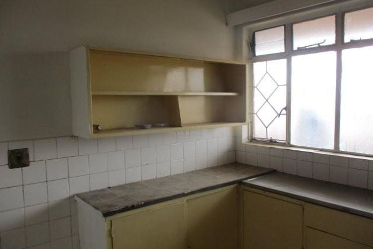 A dated kitchen area featuring original built-in cabinetry, tiled splashbacks, and laminate countertops, offering significant potential for modernization and renovation.