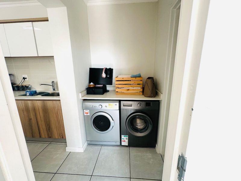 A functional laundry nook featuring a built-in countertop, tiled flooring, and adjacent kitchen cabinetry with a stainless steel sink.