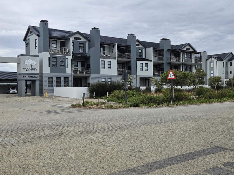 Exterior view of the Woodbury Village apartment complex entrance, featuring modern multi-story architecture with balconies and paved driveway access.
