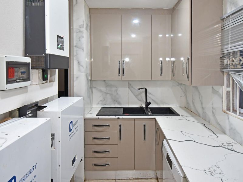 Compact scullery featuring modern gloss cabinetry, marble-look countertops, double basin sink, and integrated solar power infrastructure.