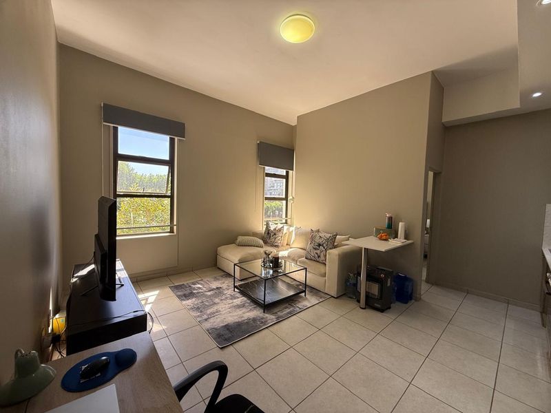 An open-plan living area featuring tiled flooring, neutral wall tones, and large windows with roller blinds, providing a bright and functional living space.