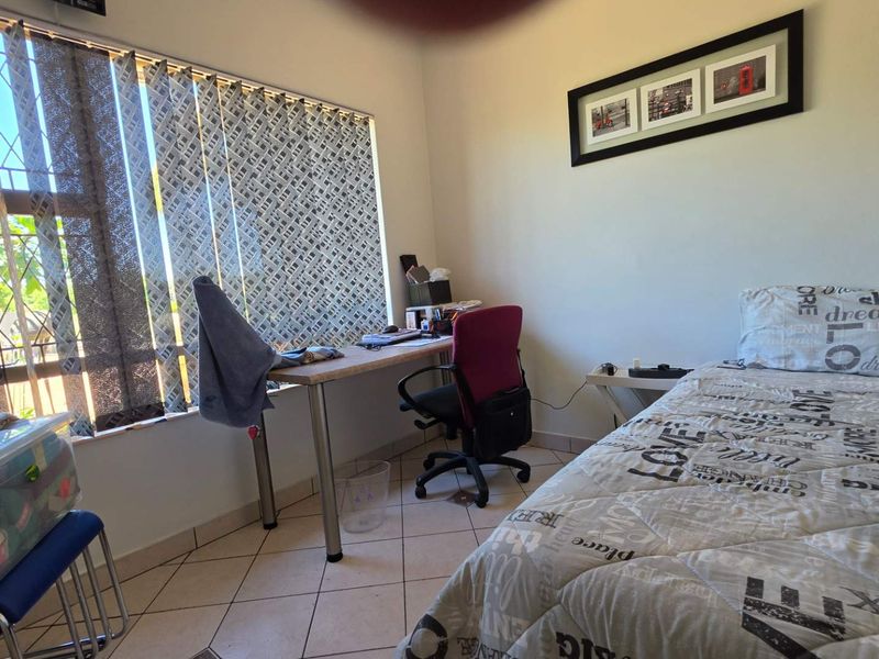 A functional bedroom featuring tiled flooring, a large window with vertical blinds, and security bars.