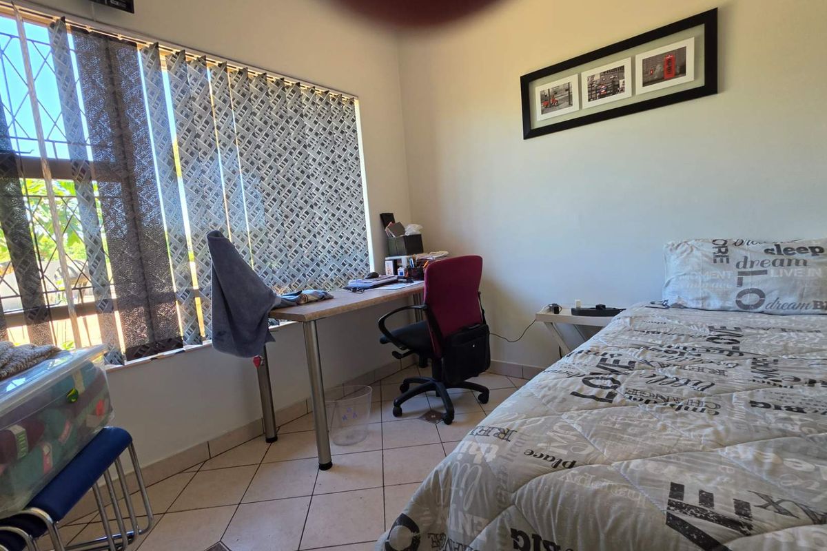 A functional bedroom featuring tiled flooring, a large window with vertical blinds, and security bars.