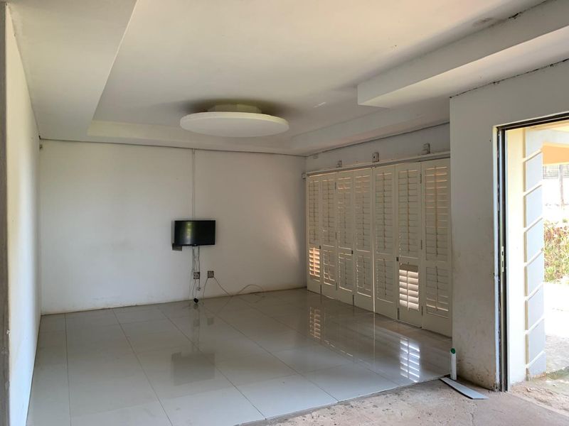 An empty living room featuring tiled flooring, a recessed ceiling, and white plantation shutters, offering a blank canvas for interior design.