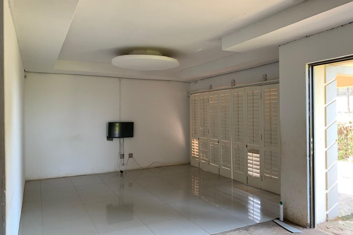 An empty living room featuring tiled flooring, a recessed ceiling, and white plantation shutters, offering a blank canvas for interior design.