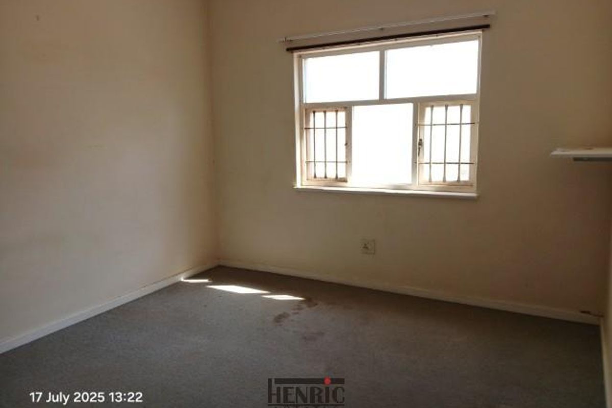 A vacant bedroom featuring neutral walls, carpeted flooring, and a window fitted with security bars.