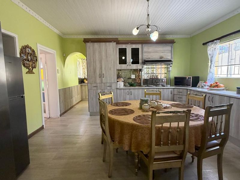 Open-plan kitchen and dining area featuring built-in cabinetry, tiled backsplash, and timber-look flooring under a classic beadboard ceiling.