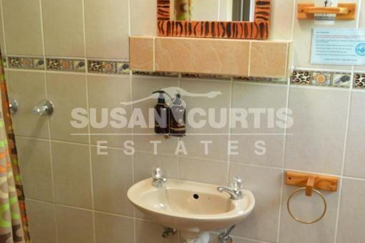 A compact bathroom featuring wall-mounted basin, tiled walls with decorative border, and a shower area with curtain.