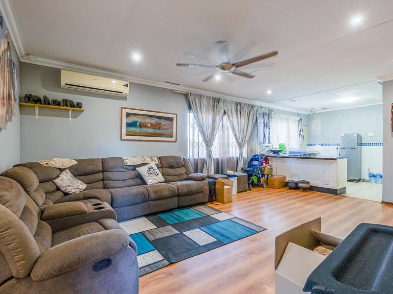 Open-plan living area featuring laminate flooring, a ceiling fan, and a connected kitchen space with a breakfast bar.