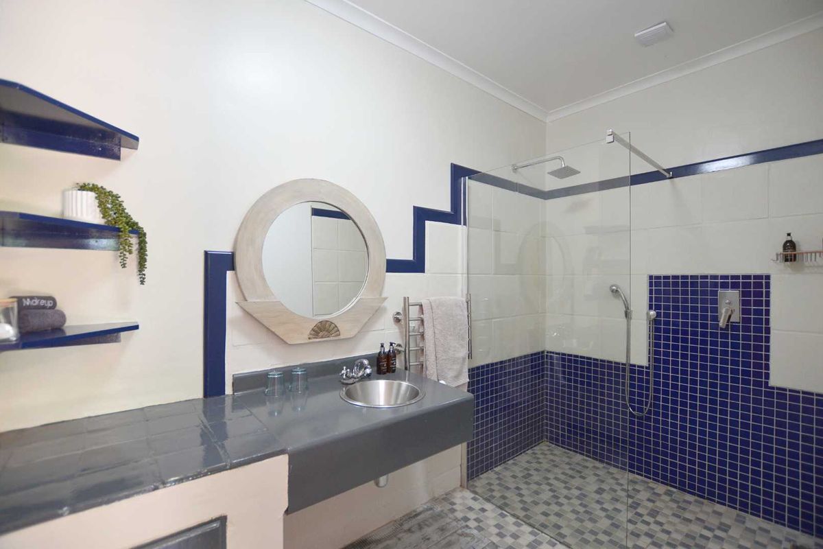 A bathroom featuring a walk-in shower with glass screen, built-in vanity with stainless steel basin, and a heated towel rail.