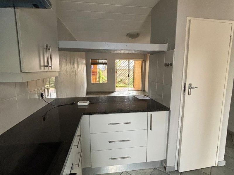 A functional kitchen featuring dark granite countertops, white cabinetry, and tiled flooring, leading into an open-plan living area with access to the outdoors.
