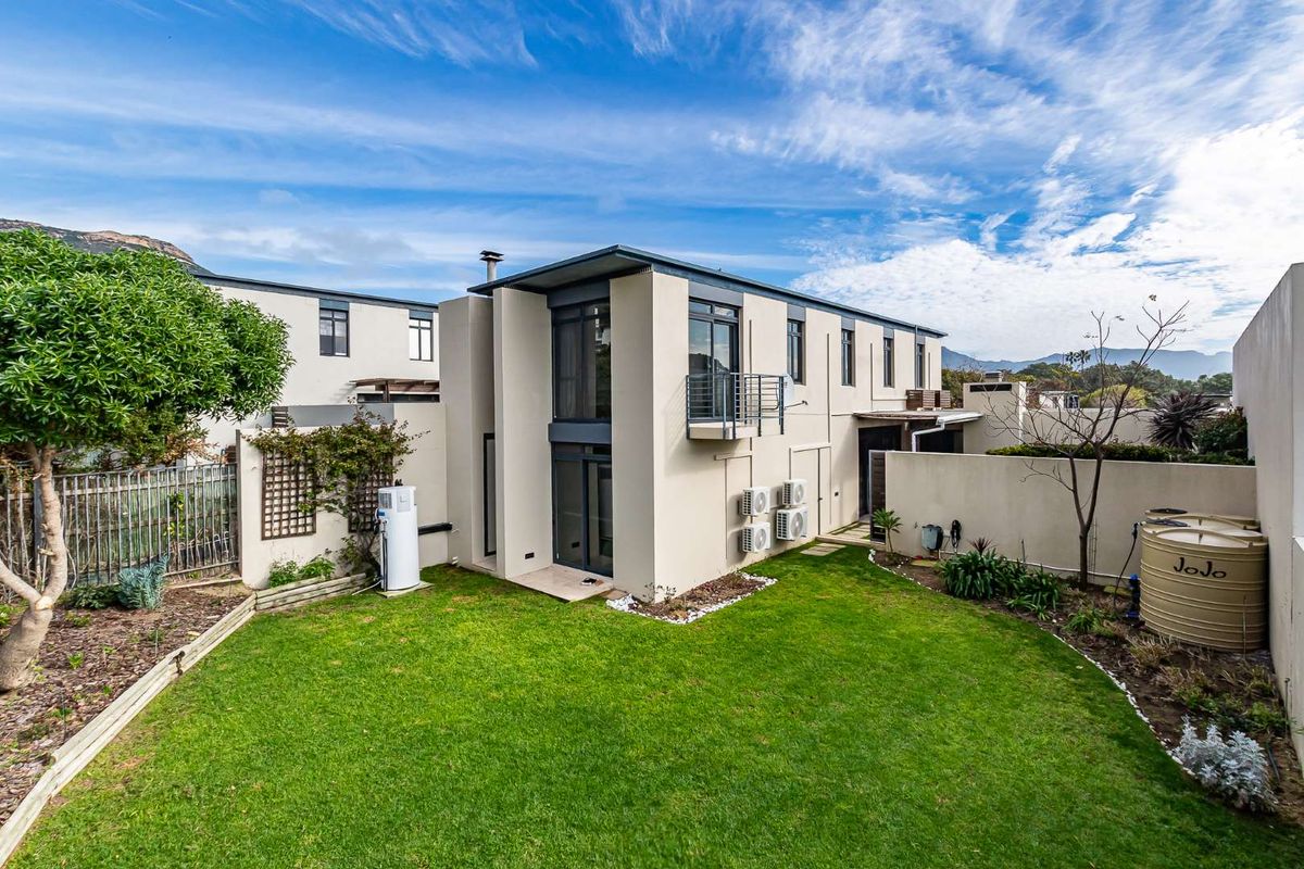 Rear view of the townhouse featuring a private garden, lawn, balcony, and exterior mounted air conditioning units.