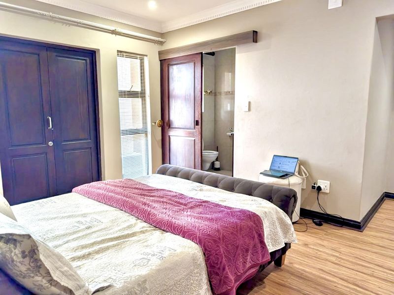 A well-maintained bedroom featuring laminate flooring, built-in cupboards, and direct access to an en-suite bathroom via a sliding door.