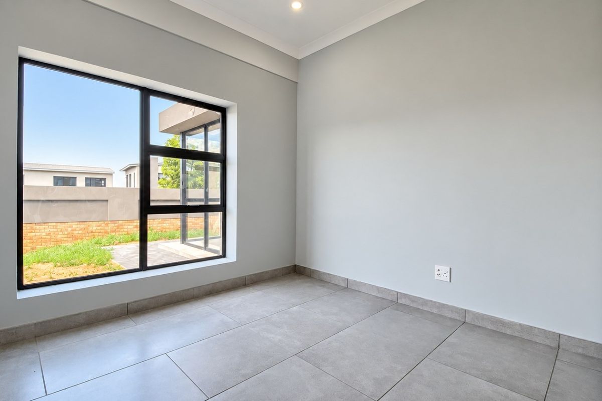 A bright, modern, and empty bedroom featuring large aluminium-framed windows, neutral tiled flooring, and built-in cupboard storage.