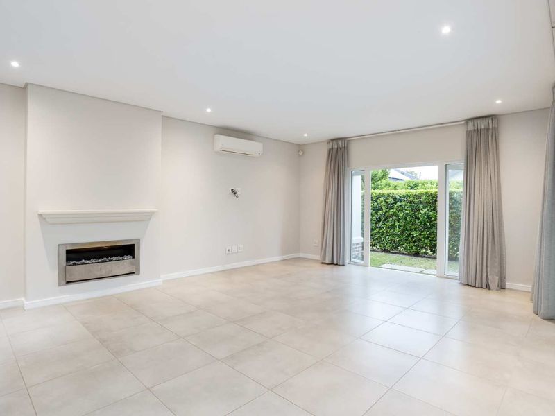 Spacious, light-filled living room featuring neutral tiled flooring, a modern recessed fireplace, split-system air conditioning, and direct access to the garden through sliding doors.