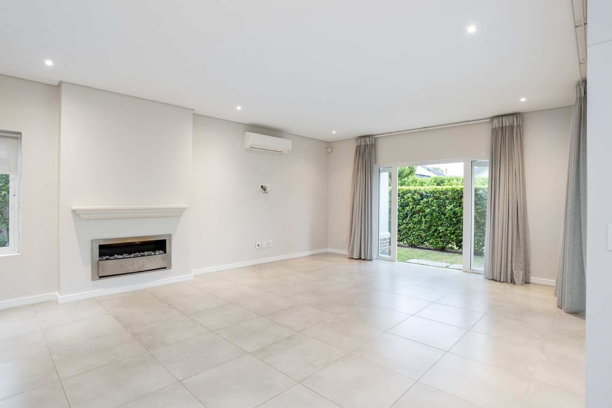 Spacious, light-filled living room featuring neutral tiled flooring, a modern recessed fireplace, split-system air conditioning, and direct access to the garden through sliding doors.