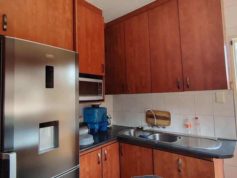 Compact kitchen featuring wood-finish cabinetry, laminate countertops, a stainless steel double sink, and a built-in microwave with direct access to an outdoor area.