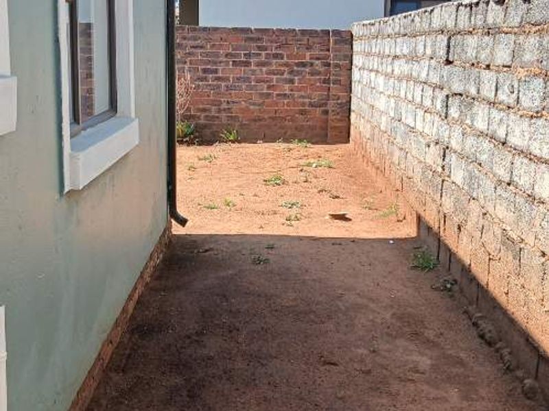 A side or rear exterior area featuring a brick boundary wall and unlandscaped ground, offering potential for garden development or paving.