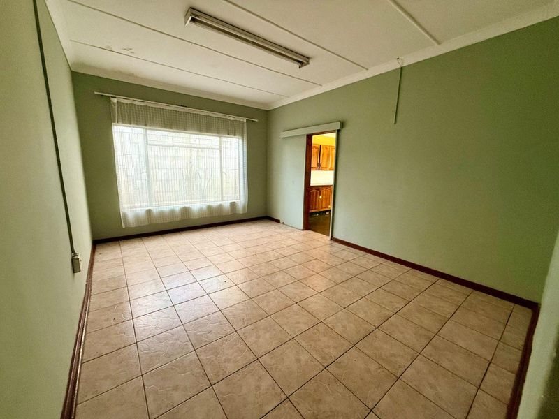 An empty living room featuring tiled flooring, a large window, and a sliding door leading to the kitchen area.