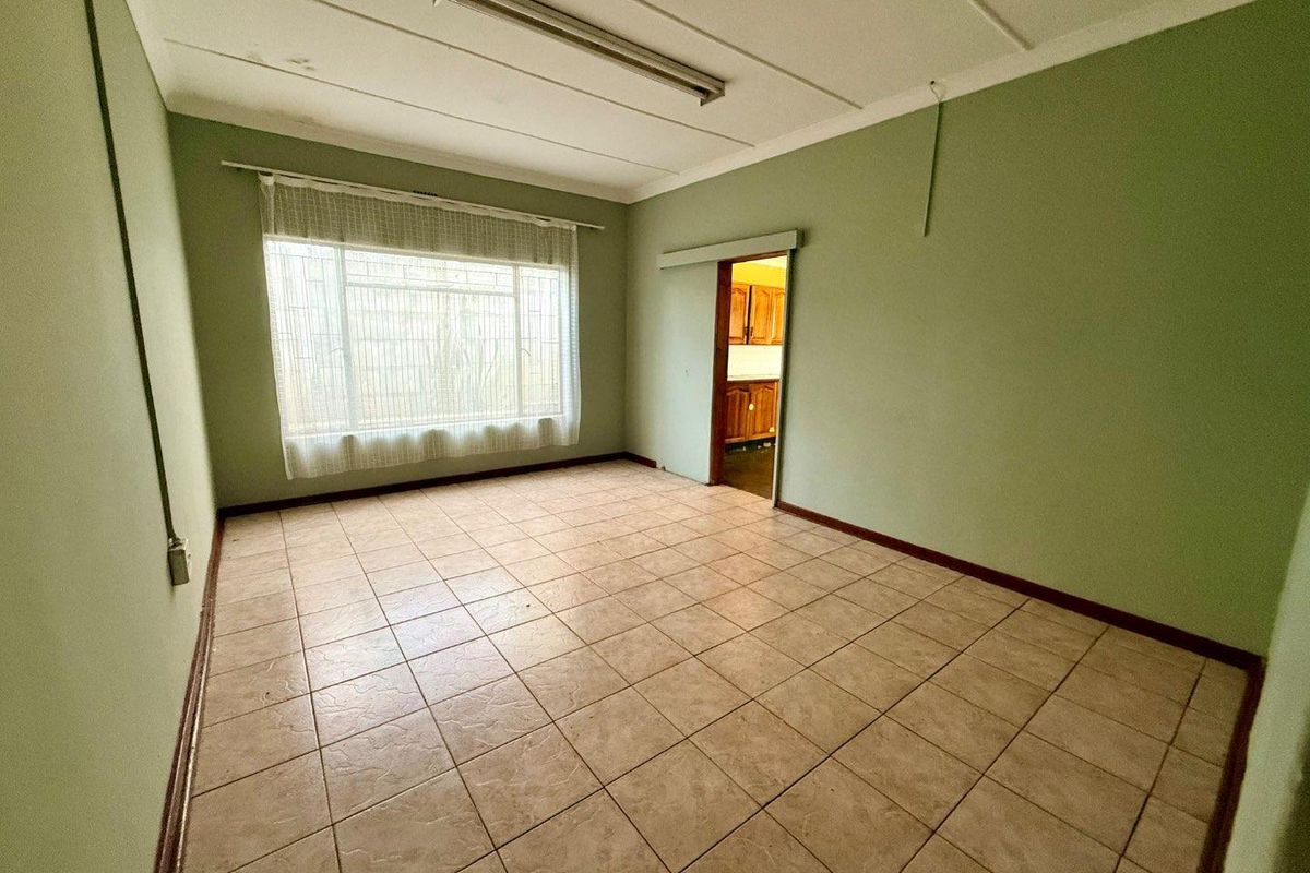 An empty living room featuring tiled flooring, a large window, and a sliding door leading to the kitchen area.