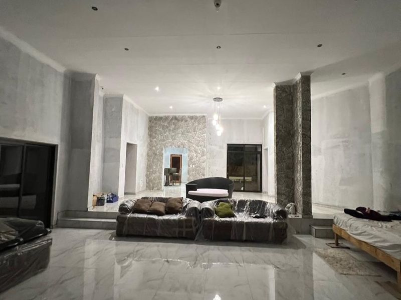 Spacious open-plan living area featuring polished marble-look flooring, recessed lighting, and a stone-clad feature wall, currently undergoing interior finishing and plastering work.