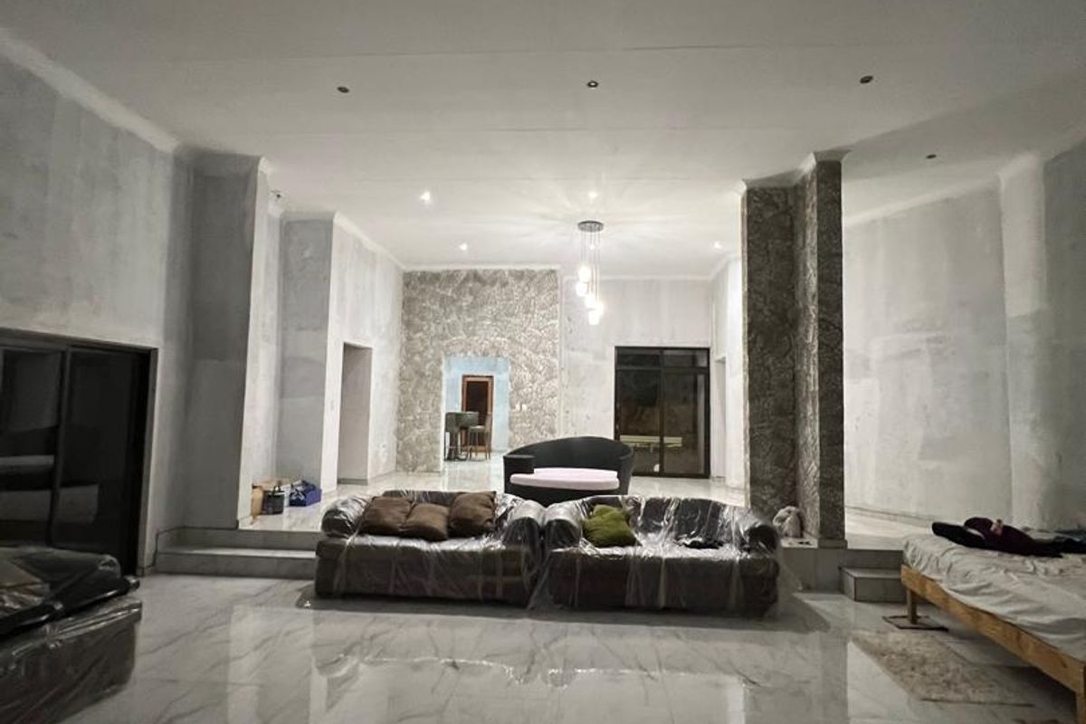 Spacious open-plan living area featuring polished marble-look flooring, recessed lighting, and a stone-clad feature wall, currently undergoing interior finishing and plastering work.