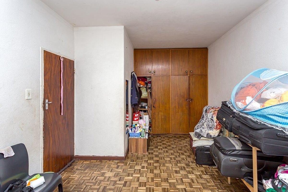 A bedroom featuring parquet flooring and built-in wooden cupboards, offering a functional layout with potential for modernization.