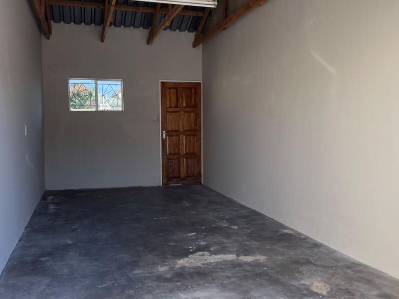 An empty, functional garage space featuring exposed timber roof trusses, a concrete floor, and a secure timber access door.