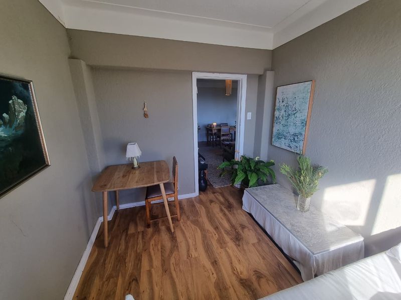 A living area featuring laminate flooring and coved ceilings, with a doorway leading to an adjacent dining space.
