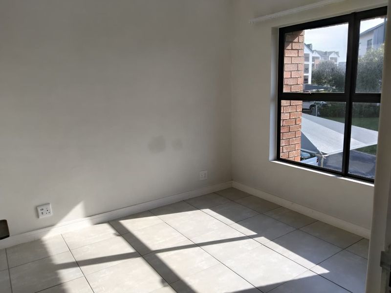 A bright, empty bedroom featuring neutral tiled flooring, a large aluminium-framed window, and clean white walls, ready for personalization.