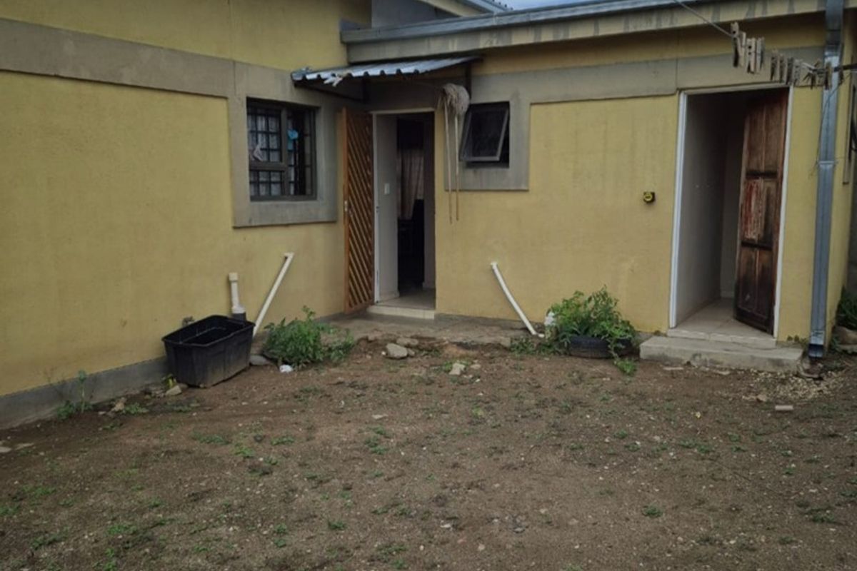 Rear exterior view of the property showing yellow painted walls, security bars on windows, and access to two separate entry points.