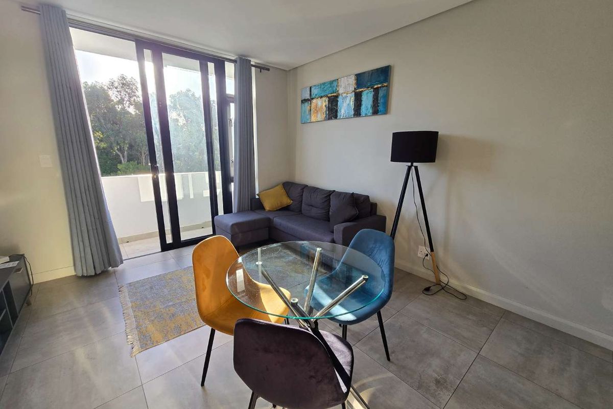 A bright living area featuring large sliding glass doors that open onto a balcony, complemented by modern tiled flooring and neutral wall finishes.