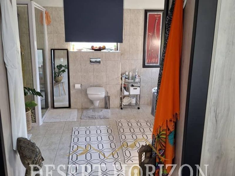 A functional bathroom featuring tiled walls and flooring, a wall-mounted toilet, and a glass shower enclosure.