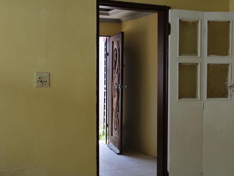 A view through a doorway showing a tiled hallway with a decorative wooden door leading to an exterior space.