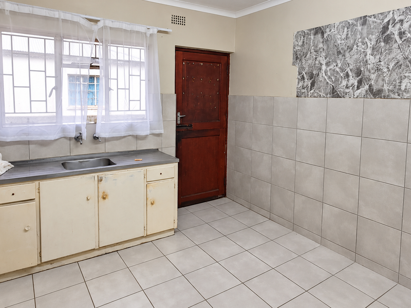 A functional kitchen space featuring tiled walls and flooring, a stainless steel sink, and built-in cabinetry, ready for modernization.