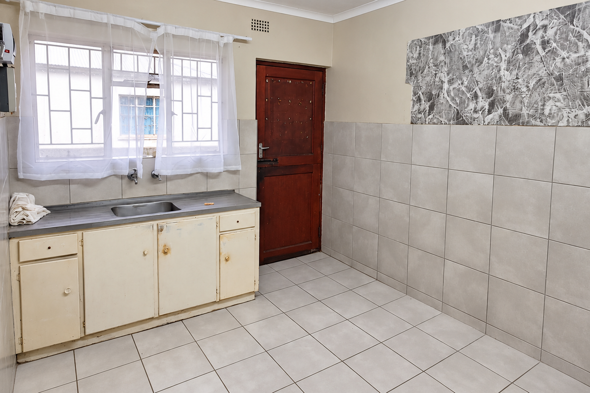 A functional kitchen space featuring tiled walls and flooring, a stainless steel sink, and built-in cabinetry, ready for modernization.