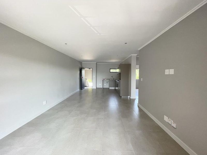 Spacious open-plan living area featuring neutral grey walls, large format floor tiles, and a compact kitchen with built-in cabinetry.