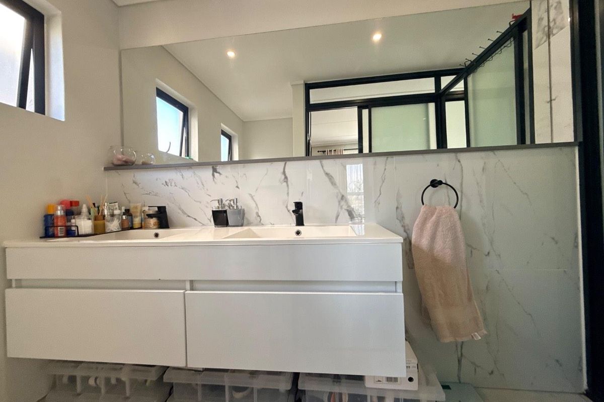 Modern bathroom featuring a double vanity with marble-look splashback, large wall-to-wall mirror, and black hardware accents.