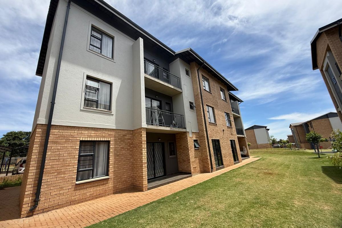 Exterior view of a modern apartment complex featuring a combination of brick and plastered finishes, private balconies, and well-maintained communal lawn areas.