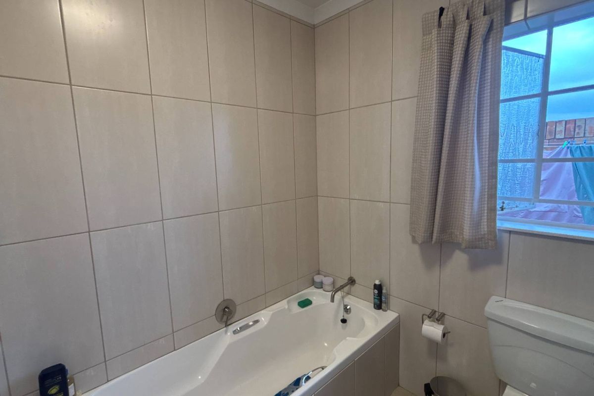 A functional bathroom featuring a built-in bathtub with wall-mounted fixtures, neutral ceramic wall tiling, and a standard toilet.