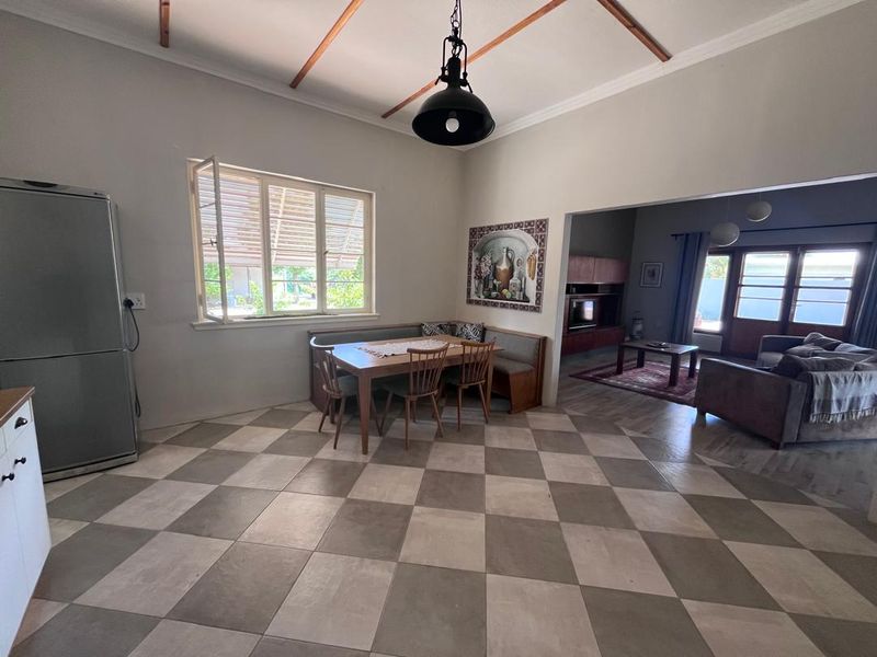 Open-plan living and dining area featuring exposed timber ceiling beams, checkered floor tiles, and a large window providing natural light.