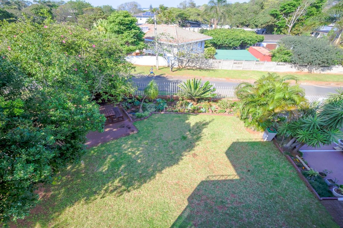 An elevated aerial view of a private residential garden featuring a well-maintained lawn, paved patio area, and established perimeter landscaping.