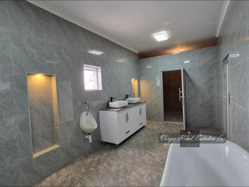 Modern, spacious bathroom featuring grey marble-look tiling, a double vanity with vessel sinks, a wall-mounted urinal, and a contemporary freestanding bathtub.