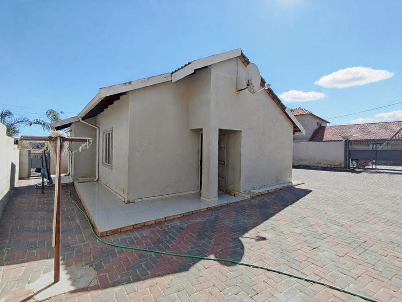 Rear view of the property featuring a paved driveway, tiled patio area, and exterior wall access with a mounted satellite dish.