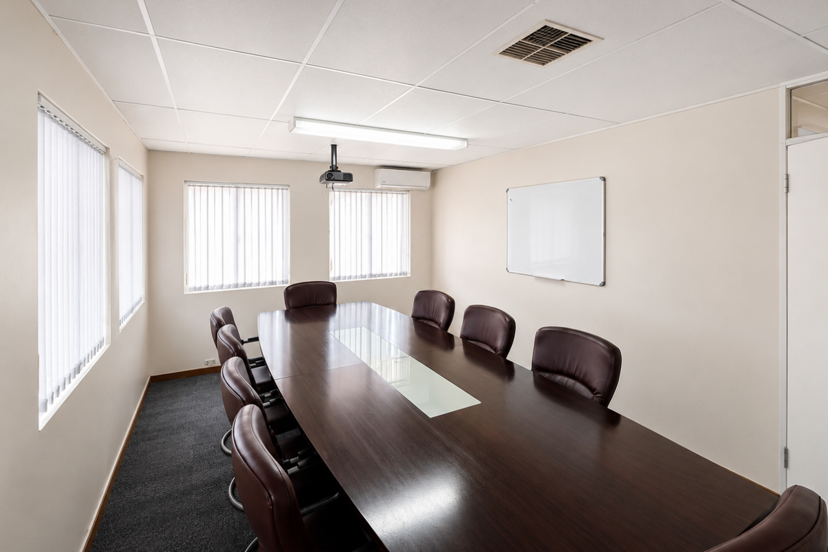 A professional office boardroom featuring a large conference table, wall-mounted whiteboard, suspended ceiling tiles, and integrated air conditioning unit.