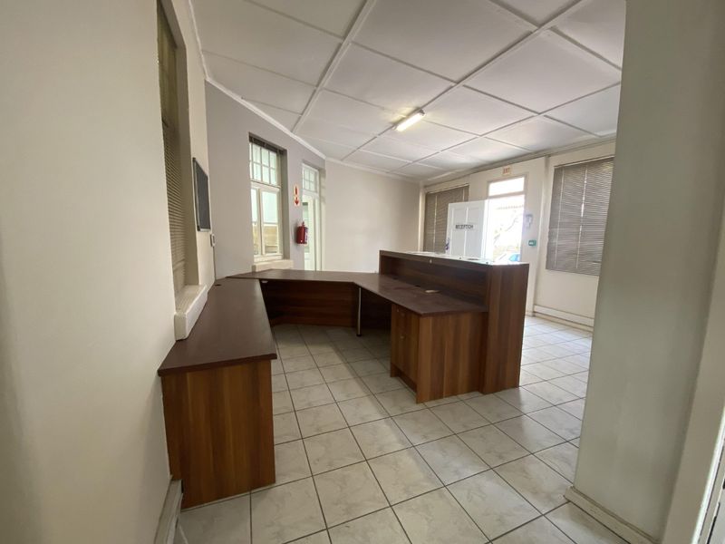 A functional office reception area featuring a built-in wooden desk, tiled flooring, and natural light through multiple windows with fitted blinds.